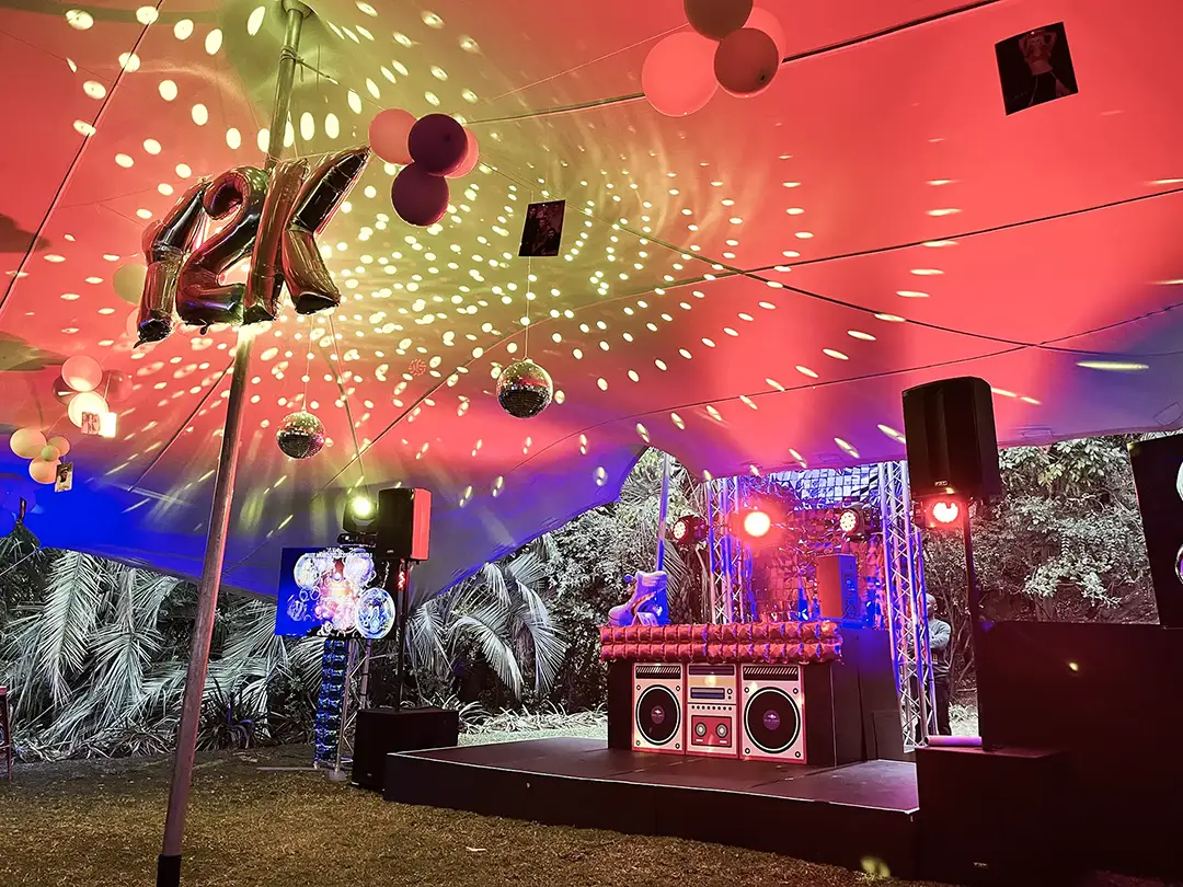 Outdoor stage under a tent with disco balls, colorful lights, and 12K silver balloons.