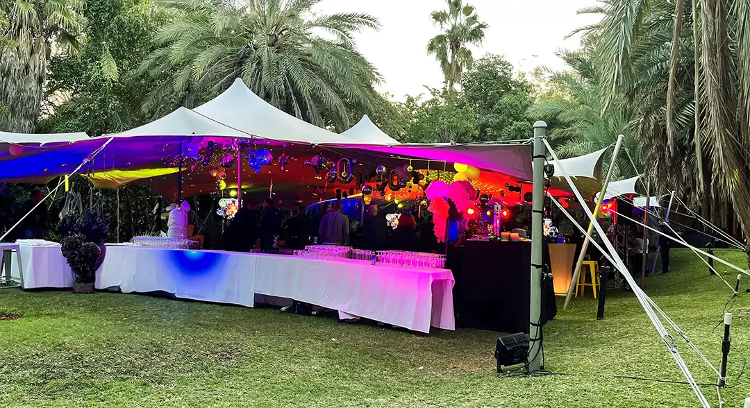 Outdoor tented event setup with colorful purple and red lighting over tables on green grass.