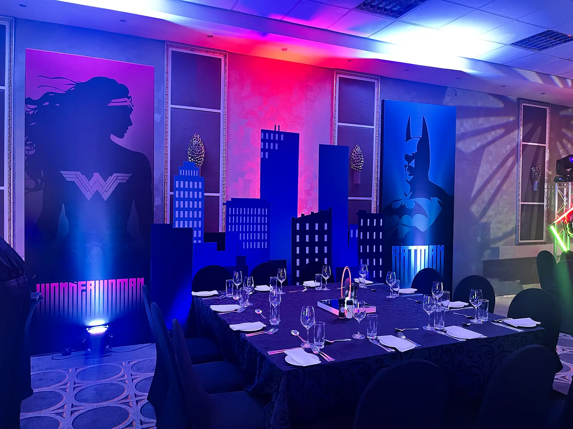 Event table set for dinner with Wonder Woman and Batman cityscape and superhero panels in background