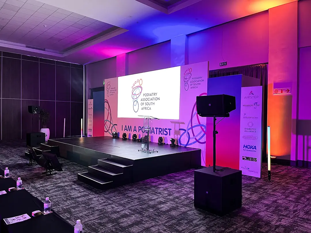 Conference stage lit with purple and orange lights, displaying Podiatry Association of South Africa logo.
